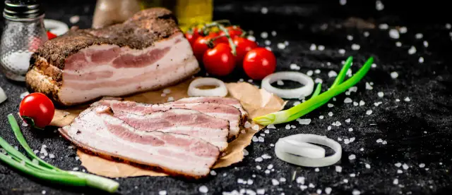 Idealny boczek do carbonary: plastry wędzonego boczku, pomidorki koktajlowe, cebula i szczypiorek na czarnym tle.