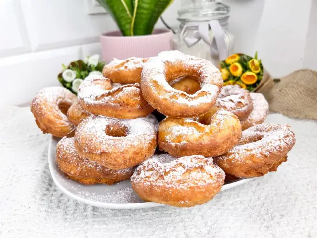 Stos puszystych, domowych oponków posypanych cukrem pudrem, gotowych do schrupania.