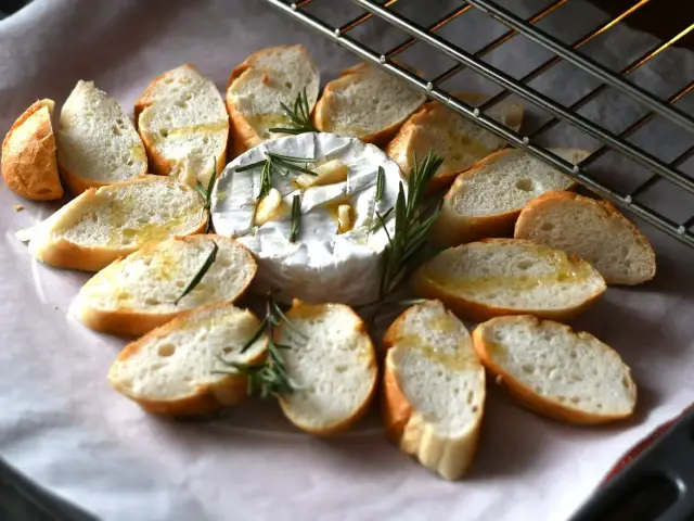 Pieczony camembert z czosnkiem i rozmarynem, otoczony kromkami bagietki, gotowy do zapieczenia.