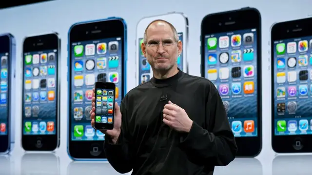 Steve Jobs prezentuje iPhone'a na tle rzędu smartfonów.