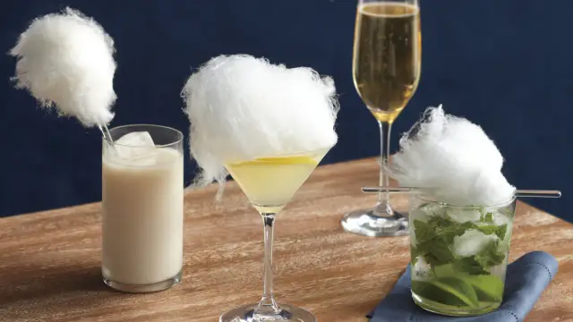 Trzy drinki z watą cukrową: biały koktajl, martini z cytryną i mojito. Obok kieliszek szampana.