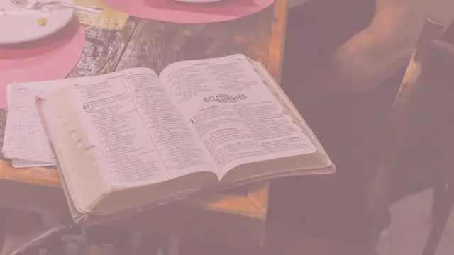 Otwarta księga Koheleta, tekst biblijny, leży na stole obok notatek.