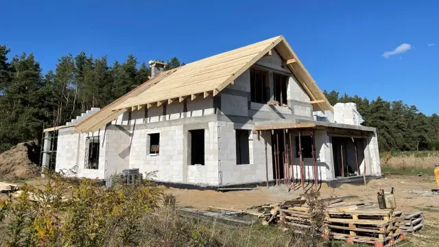 Budowa domu z bloczków, z widocznym szkieletem dachu. To początek realizacji indywidualny projekt domu w otoczeniu lasu.