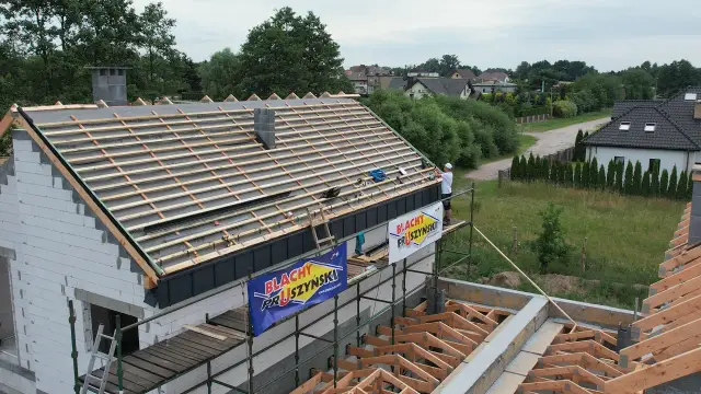 Budowa dachu z widoczną **powłoką antykondensacyjną** i pracownikiem na rusztowaniu.