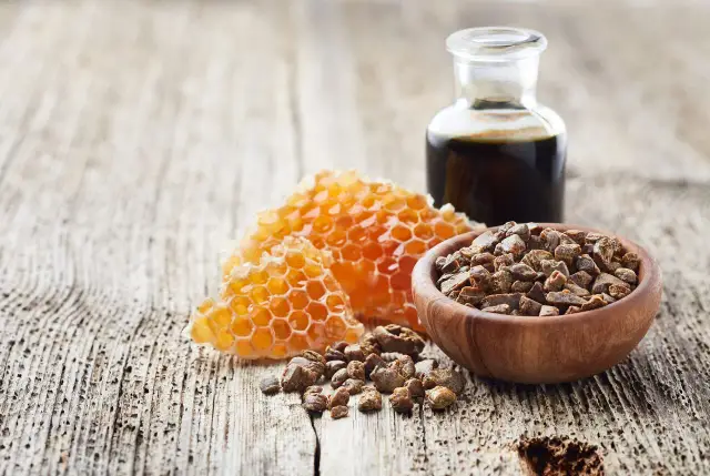 Propolis działanie: miód, plastry miodu, propolis w ziarnach i nalewka na drewnianym tle.