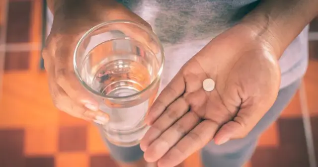 Dłoń trzyma szklankę wody i tabletkę. Uważaj, paracetamol dawka śmiertelna jest niebezpieczna.