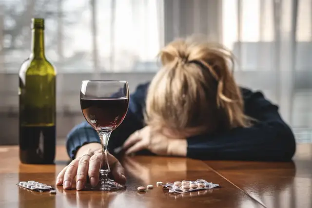 Kobieta z opuszczoną głową obok kieliszka wina i leków. Niebezpieczne połączenie escitalopram a alkohol.