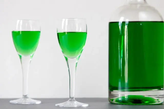 Dwa kieliszki i butelka wypełnione jaskrawozielonym likierem miętowym, idealne do domowego przepisu na zielony likier miętowy typu creme de menthe.
