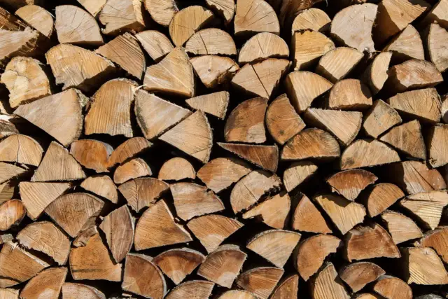 Stos drewna opałowego, idealnego na pytanie: jakie drewno do kominka? Widać słoje i pęknięcia, świadczące o jego naturalnym pochodzeniu.