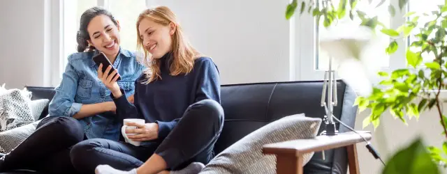 Dwie przyjaciółki śmieją się, oglądając coś na telefonie. Idealny pomysł na to, co można robić z bff w domu.
