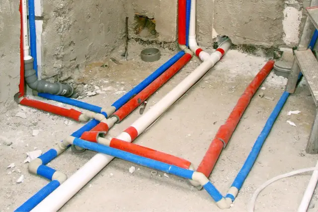 Skomplikowana instalacja hydrauliczna z rurami w kolorach czerwonym, niebieskim i białym. Trudno od razu stwierdzić, z której strony ciepła woda.