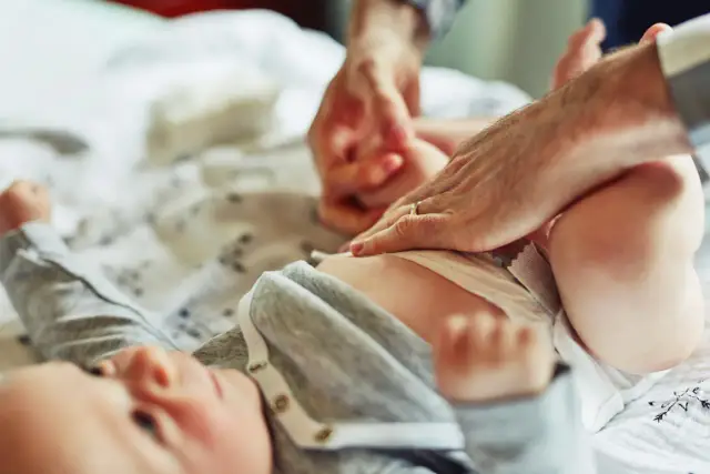 Rączki rodzica zmieniają pampersa noworodkowi. Ile noworodek zużywa pampersów? To pytanie nurtuje wielu rodziców.