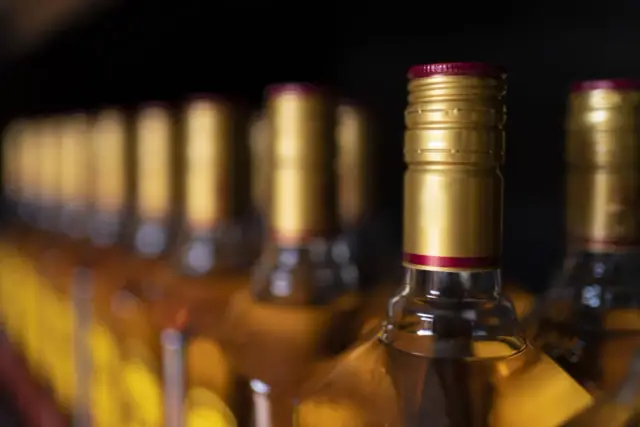 Rząd butelek z alkoholem, z błyszczącymi złotymi zakrętkami. Zastanawiasz się, czy można przewozić alkohol w bagażu rejestrowanym?