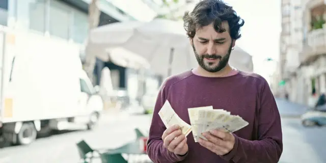 Mężczyzna liczy banknoty, zastanawiając się nad cenami w Kopenhadze.