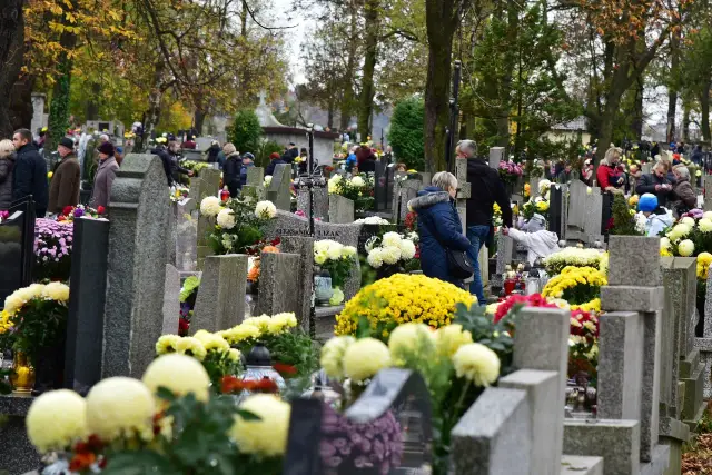 Ludzie odwiedzają cmentarz komunalny w Wieliczce, składając kwiaty i zapalając znicze.