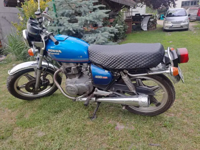 Niebieski motocykl Honda CB250T z pikowanym siedzeniem stoi na trawie.