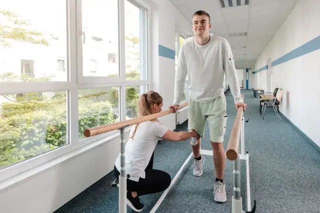 Fizjoterapeutka pomaga pacjentowi przy poręczy. Dowiedz się, jak uzyskać świadczenie rehabilitacyjne po ustaniu zatrudnienia.