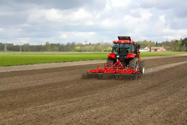 Czerwony traktor z agregatem uprawowym na polu. Przygotowanie gleby pod zasiew, jak wniosek o przedłużenie umowy dzierżawy kowr wzór.
