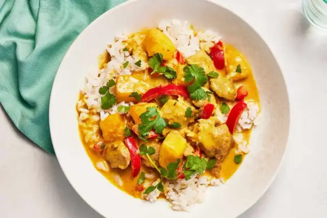 Aromatyczny kurczak curry z ryżem, papryką i kolendrą, podany w białej misce.