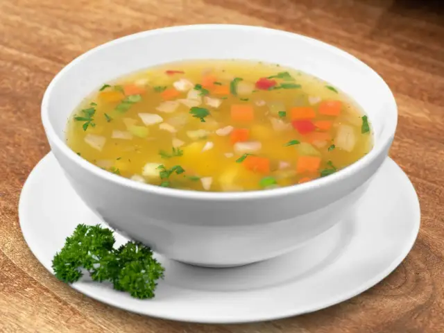 Aromaticzna jarzynowa zupa z kawałkami marchewki, ziemniaków i zielonej pietruszki w białej misce na drewnianym tle.