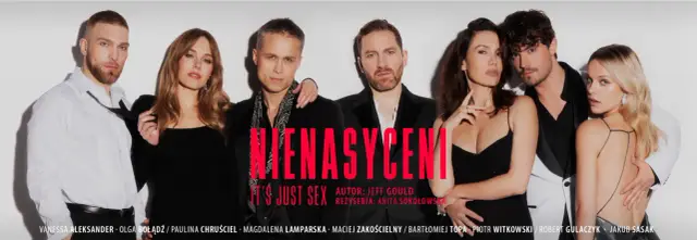 Nienasyceni spektakl: siedem osób w eleganckich strojach, w tym cztery kobiety i trzech mężczyzn, pozuje do zdjęcia.
