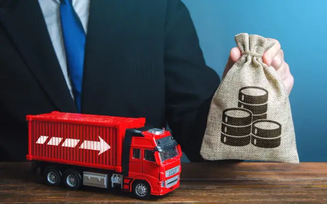 Biznesmen z workiem pieniędzy i czerwona ciężarówka symbolizują, jak optymalizować koszty transportu w handlu towarami masowymi.