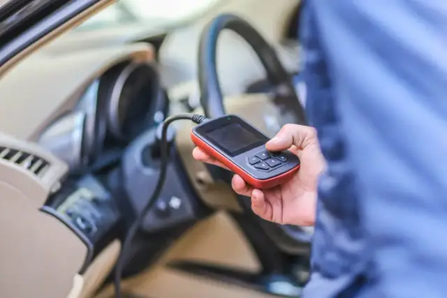Diagnostyka Renault, być może błąd DTC B1267. Ręka trzyma skaner OBD-II przy kierownicy.