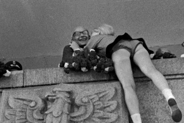 22 lipca. Uśmiechnięty mężczyzna w okularach obejmuje dziewczynę, która kładzie mu głowę na ramieniu. W tle widać wieniec.