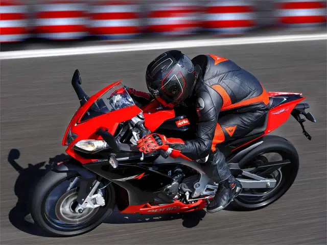 Motocyklista w kombinezonie śmiga na torze na czerwono-czarnej Aprilia RS4.