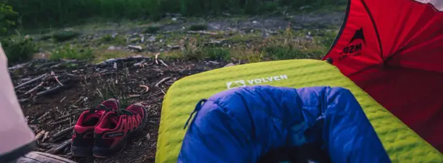 Czerwone buty Salomon i niebieski śpiwór leżą na zielonej kalimacie obok namiotu.