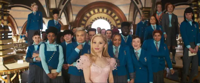 Ariana Grande w różowej sukience wśród uczniów w niebieskich mundurkach. Scena z jednego z jej filmów.