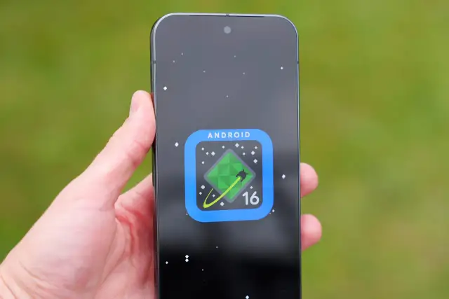 Dłoń trzyma smartfon z ikoną Android 16 na czarnym tle z gwiazdami.