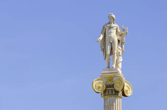 Kamienna rzeźba Apollina, brata Artemidy, z lirą w dłoni, na ozdobnej kolumnie pod błękitnym niebem.