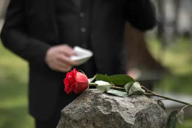 Czerwona róża na kamieniu, w tle osoba w czerni. Trudne chwile, gdy szukamy informacji, gdzie jest najbliższe krematorium.