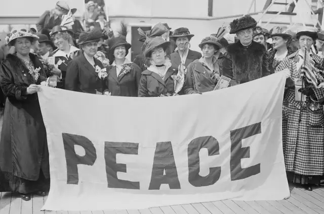 Kobiety z transparentem "PEACE" symbolizują emancypację kobiet i pozytywizm, dążąc do pokoju i równości.
