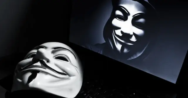 Maska Guy Fawkes leży na klawiaturze obok ekranu z podobną maską. Symbolizuje anonimowego hakera.