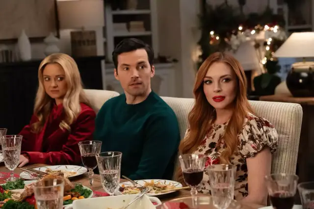 Lindsay Lohan w świątecznej komedii. Trzy osoby siedzą przy stole, na którym jest jedzenie.