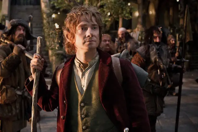 Bilbo Baggins, z charakterystyką hobbita, wyrusza w podróż. W tle widać innych hobbitów i krasnoludów.