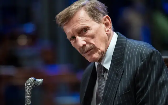 Jan Englert w eleganckim garniturze, z charakterystyczną laską z głową psa. Wiele jego ról w **jan englert filmy** zapisało się w historii polskiego kina.