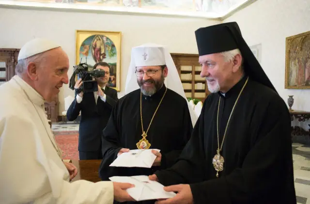 Papież Franciszek wita grekokatolickiego arcybiskupa, wręczając sobie nawzajem koperty.