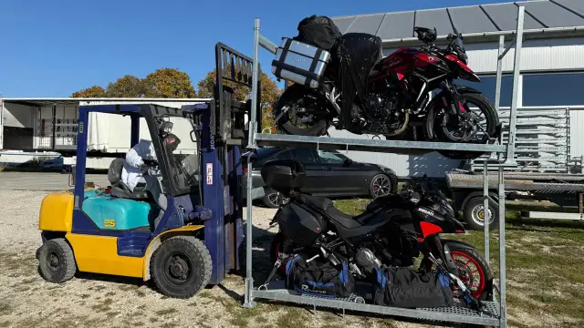Wózek widłowy przygotowuje transport motocykla. Dwa motocykle na stojaku, jeden czerwony, drugi czarny.