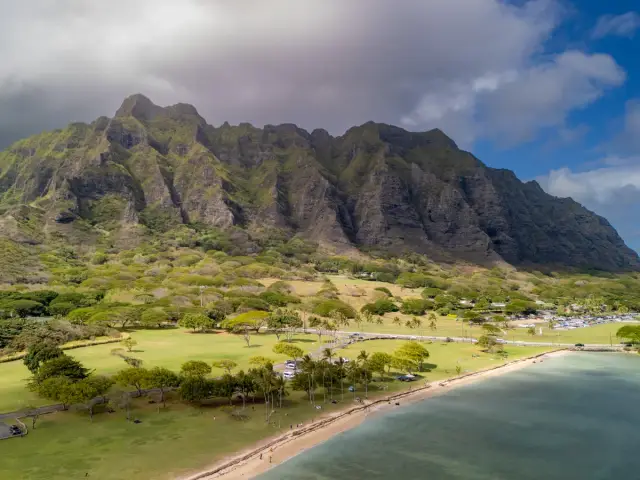 Majestatyczne góry Ko'olau górują nad zielonymi polami i plażą, przypominającymi krajobraz z **Waikiki**.
