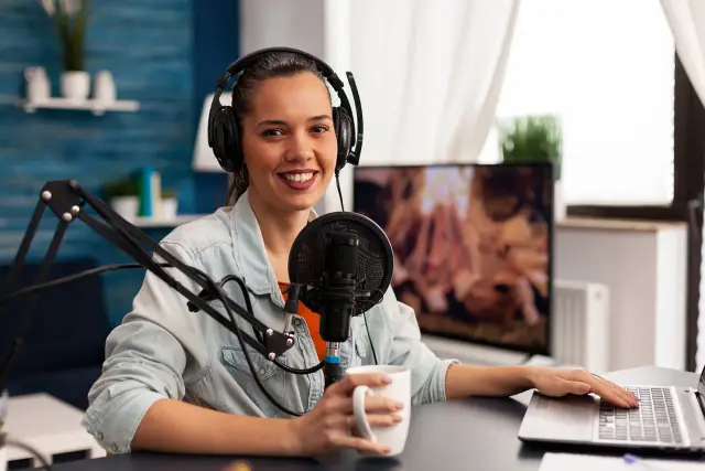 Uśmiechnięta dziewczyna w słuchawkach przy mikrofonie, tworzy podcast. To jej szkolny radiowęzeł, gdzie nagrywa ciekawe materiały.