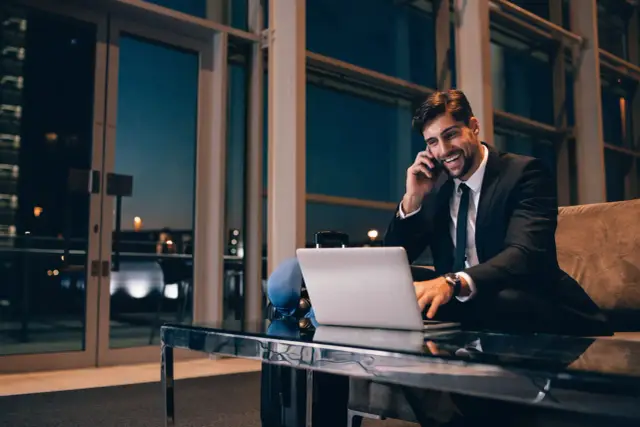 Biznesmen rozmawia przez telefon, pracując przy laptopie. Dowiedz się, kiedy przysługuje ryczałt za nocleg w delegacji krajowej i ile wynosi.