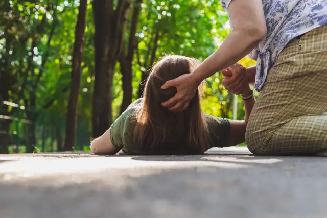 Ktoś doświadcza ataku padaczki na ścieżce w parku, druga osoba próbuje pomóc.