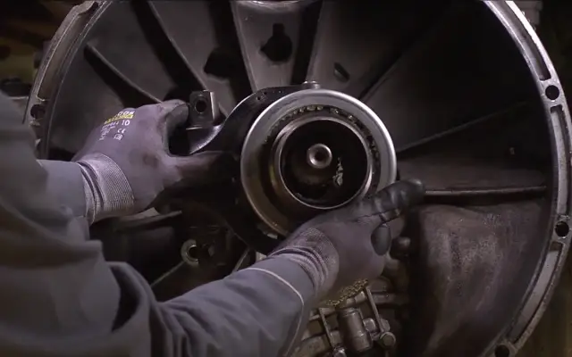 Mechanik w rękawicach wymienia łożysko oporowe w skrzyni biegów.