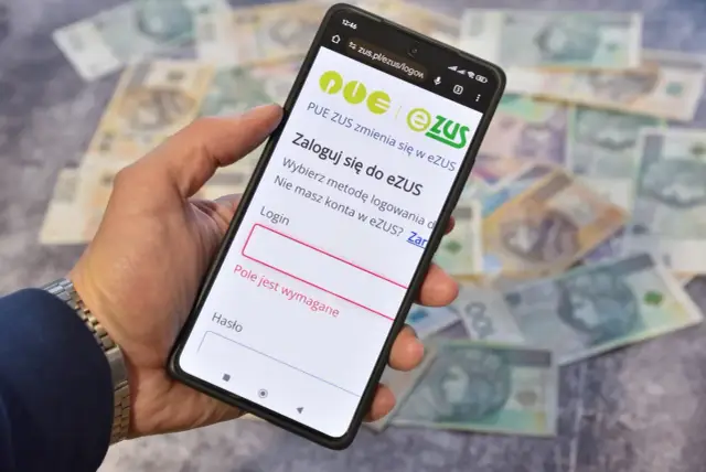 Dłoń trzyma smartfon z ekranem logowania do eZUS, na tle rozłożonych polskich banknotów.