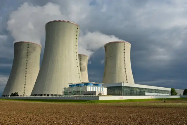 Chłodnie kominowe elektrowni jądrowej, symbolizujące energię dla Europy, wydzielają parę na tle burzowego nieba. **Euratom** wspiera takie inwestycje.