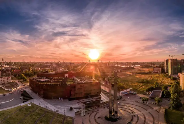 Zachód słońca nad placem Solidarności w Gdańsku. Monumentalne krzyże i nowoczesna architektura w blasku złotej godziny.