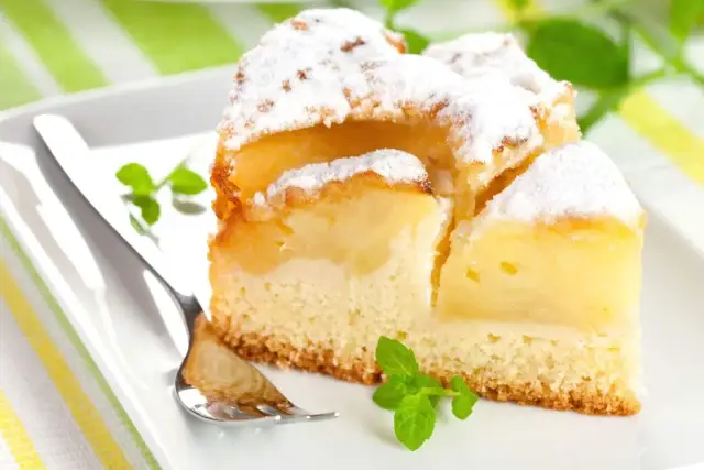 Pyszne, mega szybkie ciasto na oleju z jabłkami, posypane cukrem pudrem, na białym talerzu z miętą i widelcem.